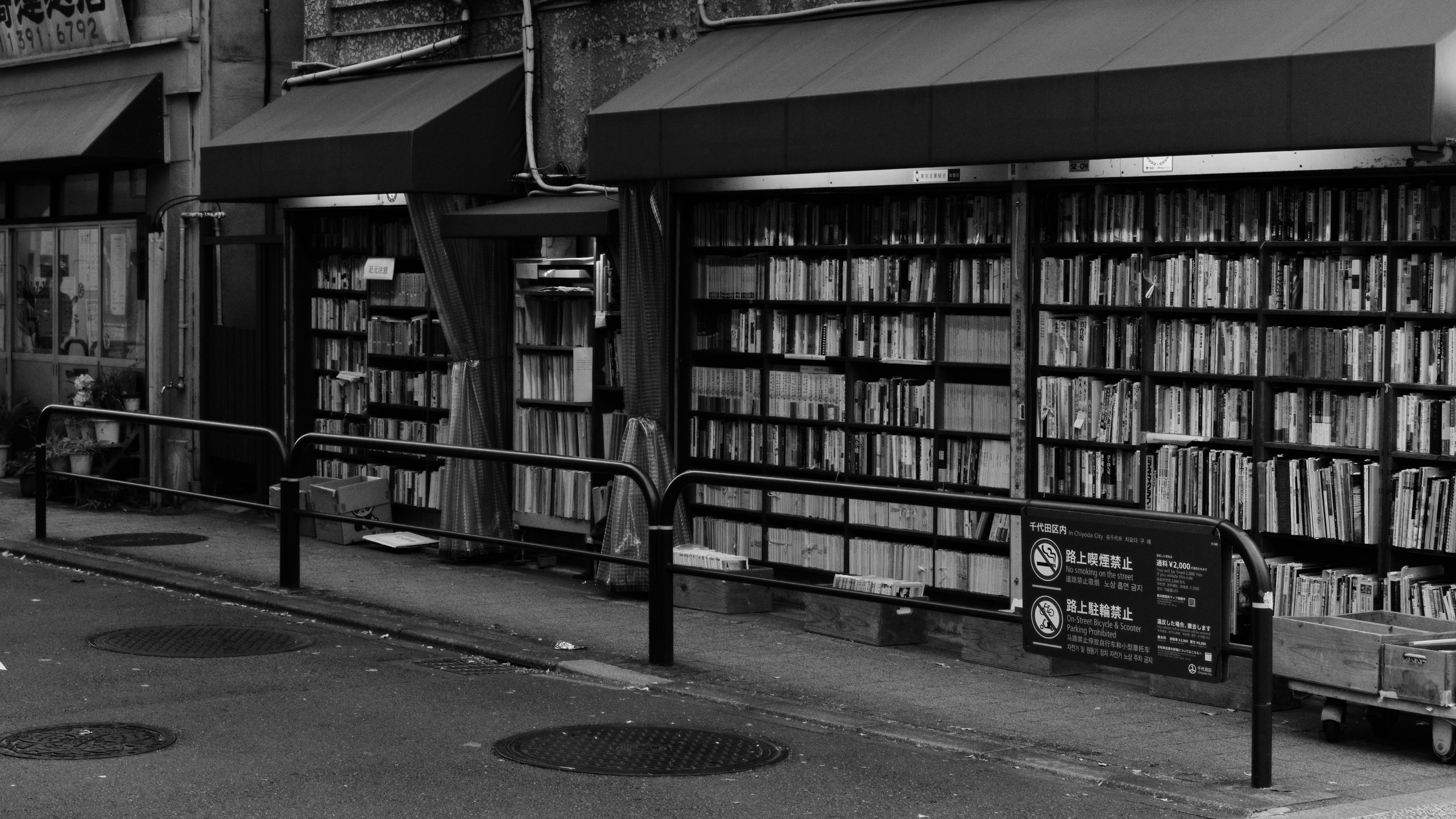 A black and white shot of a Tokyo bookstore with filled bookshelves on its outside wall.